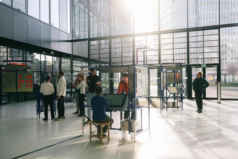 Eine Besuchergruppe versammelt sich um die Ausstellungsstationen in einem sonnendurchfluteten, verglasten Atrium.